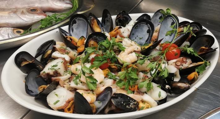 Un piatto ovale di cozze, gamberi, calamari e polpo sul banco d'acciaio, con i pesci interi dietro