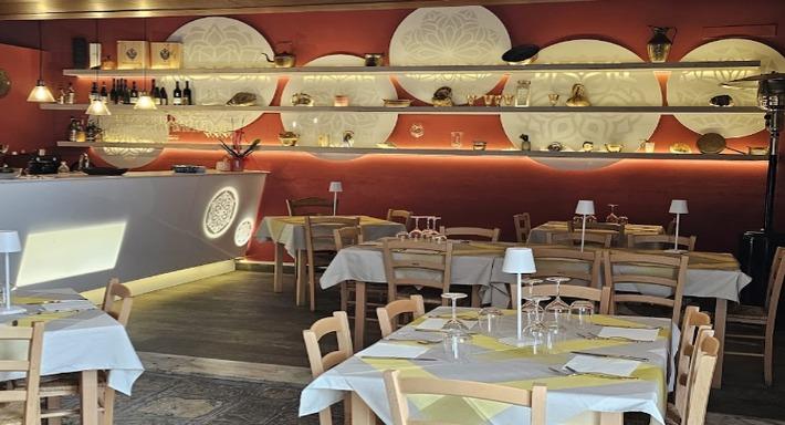La sala: parete color terracotta, grandi dischi bianchi intagliati sulle mensole illuminate, tavoli bianchi con la striscia gialla