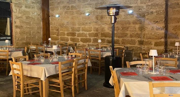 La stessa sala la sera, muro di tufo illuminato, tovaglie bianche con le tovagliette rosse