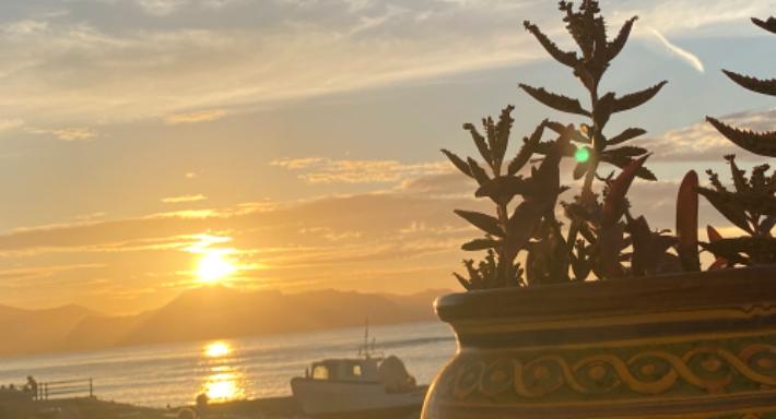 Il sole che cala sul golfo, una barca da pesca in secca sulla spiaggia e un vaso di maiolica in primo piano